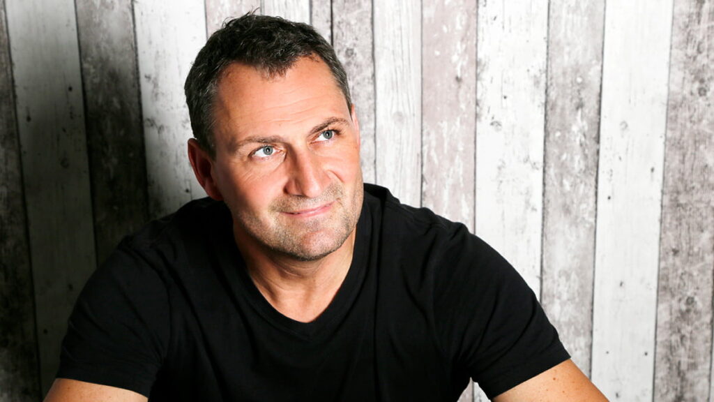 Herr Brockhaus von mediraum design in schwarzem T-Shirt vor einer grauen Wand mit Blick nach oben und leichtem Lächeln