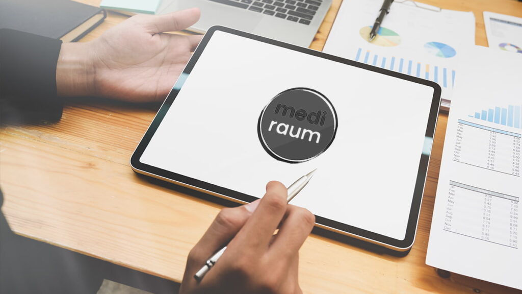 Tablet mit mediraum-Logo liegt in einer Hand, während eine zweite Hand einen Sift hält und Zettel liegen auf dem Tisch